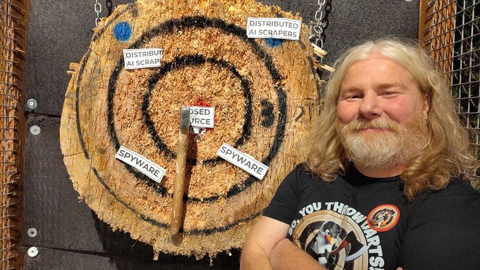 Il volontario Marcello Masotto, detto "il Vichingo" mostra il suo ceppo di legno, colpito dalla sua ascia, mentre ha fatto centro con il tiro con l'ascia, colpendo la parola "closed source". Ci sono altre parole come "distributed AI scrapers" e "spyware" da colpire